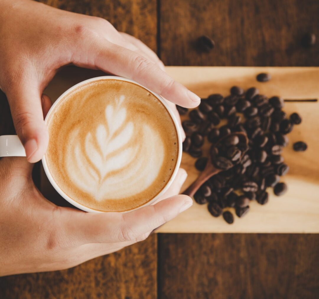 mano sosteniendo taza de cafe con granos de café al fondo